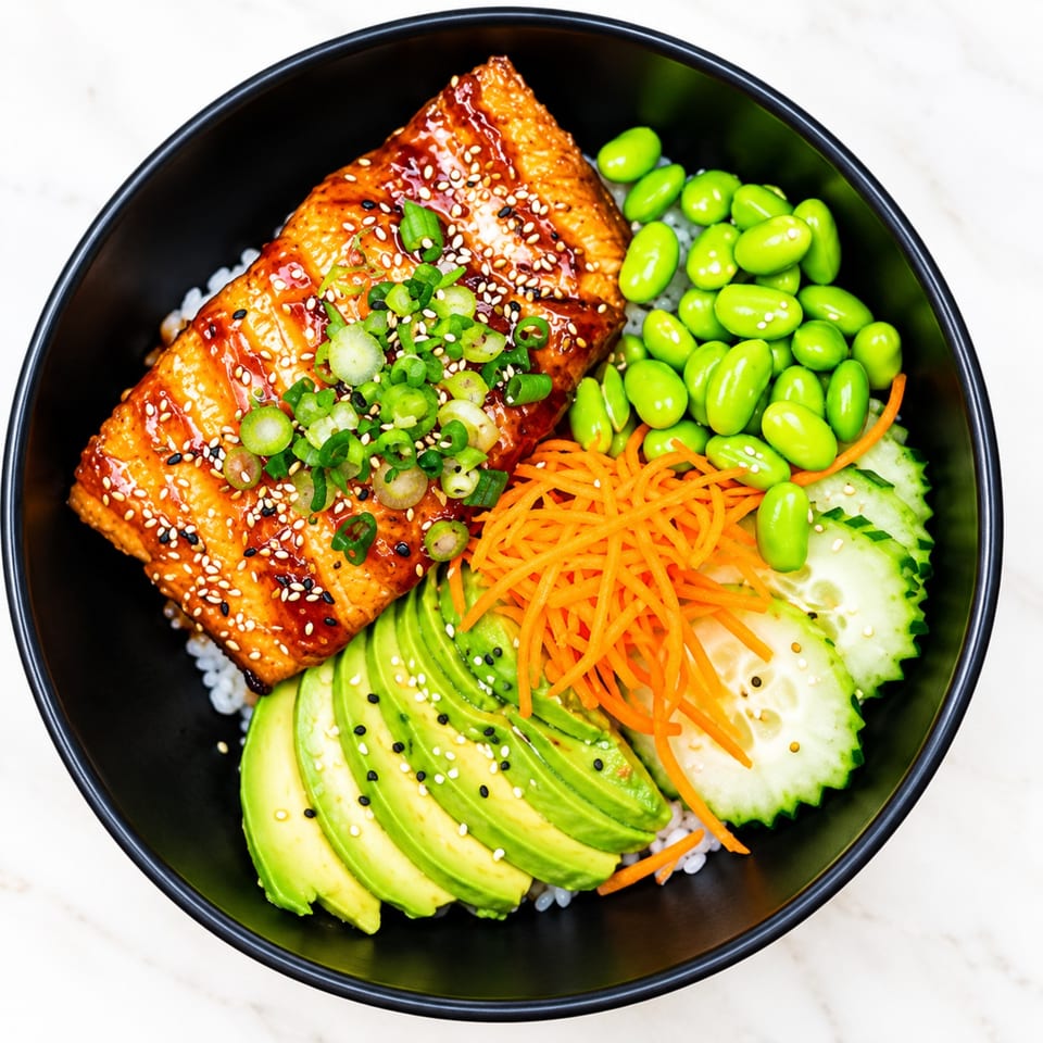 Teriyaki-glazed salmon rice bowl topped with sesame seeds and scallions, served with edamame, avocado, carrots, and cucumber.